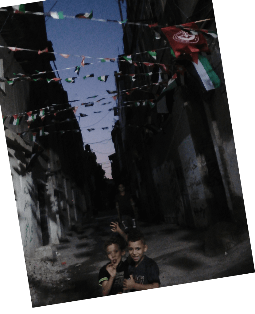 two children making faces under Palestine's flag in alley